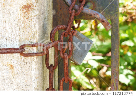 Old corroded padlock on a rusty chain hanging on a closed ancient garden gate Old corroded padlock on a rusty chain hanging on a closed ancient garden gate 117213774