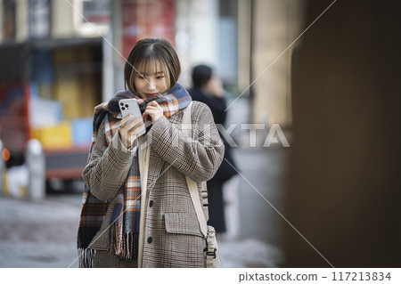 Smiling young woman looking at her smartphone in the city Smiling young woman looking at her smartphone in the city 117213834