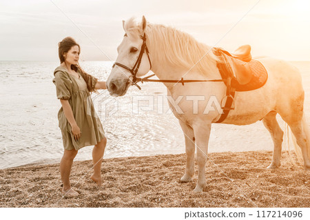 A white horse and a woman in a dress stand on a beach, with the A white horse and a woman in a dress stand on a beach, with the 117214096