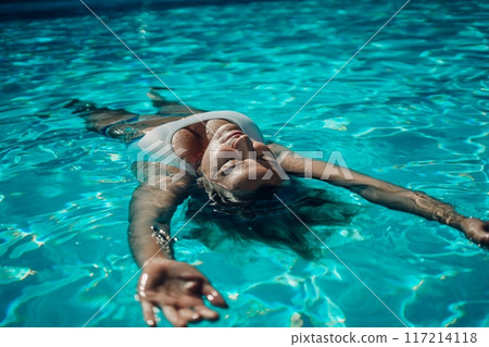 Woman relaxing swimming pool. Happy woman in a blue swimsuit floating in the pool, look form above 117214118