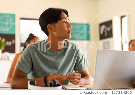 In high school, teenage boy attentively listening in classroom with laptop on desk In high school, teenage boy attentively listening in classroom with laptop on desk 117214200