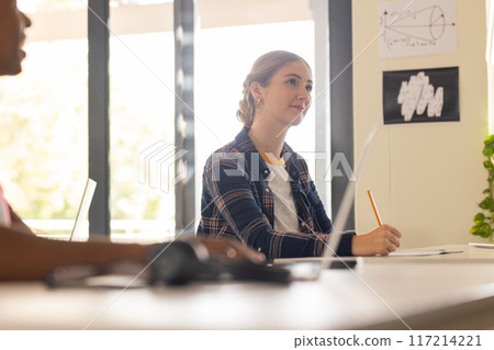 In high school, teenage girl taking notes in classroom, listening attentively 117214221