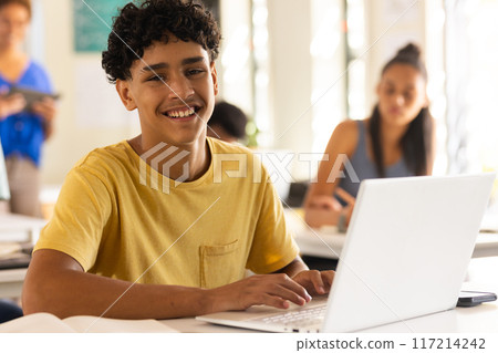 Smiling teenage boy using laptop in high school classroom, engaging in learning activities Smiling teenage boy using laptop in high school classroom, engaging in learning activities 117214242