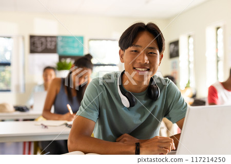 In high school, teenage boy smiling with headphones around neck in classroom 117214250