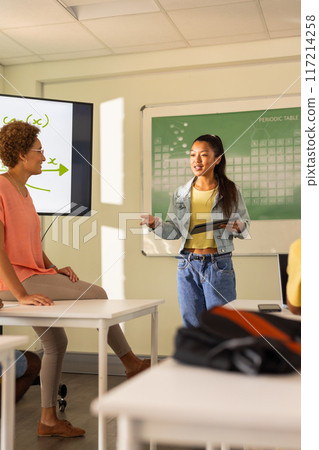 In high school, teenage girl presenting with tablet in classroom, engaging with teacher 117214258
