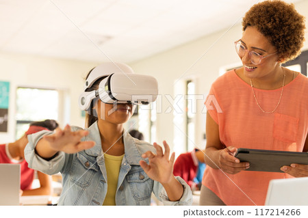 In high school, student using VR headset while teacher with tablet watching In high school, student using VR headset while teacher with tablet watching 117214266