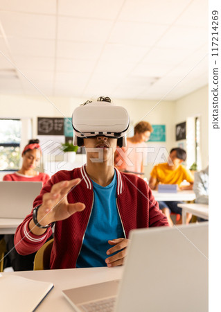 In high school, teenage boy using VR headset and laptop in classroom, exploring technology 117214269