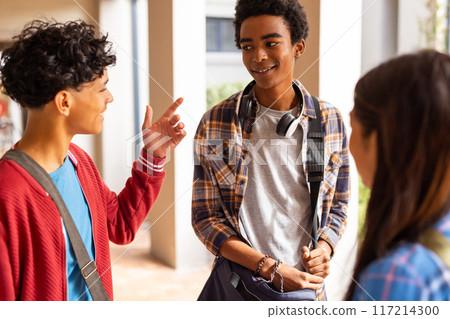 Teenagers talking and smiling, wearing backpacks and headphones at high school Teenagers talking and smiling, wearing backpacks and headphones at high school 117214300
