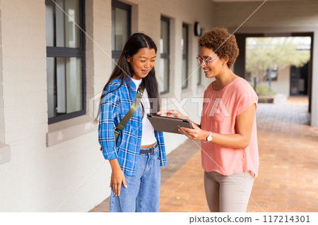 In high school, teacher showing tablet to student in hallway, discussing work 117214301