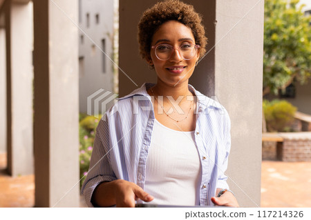 Smiling teenager in high school holding tablet, standing outside classroom building Smiling teenager in high school holding tablet, standing outside classroom building 117214326