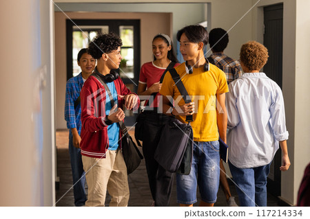 Teenagers walking in high school hallway, talking and carrying backpacks and books Teenagers walking in high school hallway, talking and carrying backpacks and books 117214334
