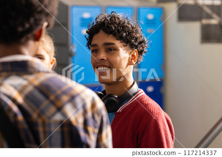 Smiling teenage boy with headphones talking to friends in high school hallway Smiling teenage boy with headphones talking to friends in high school hallway 117214337