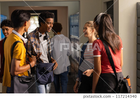 Teenagers in high school hallway talking and laughing, holding books and backpacks 117214340