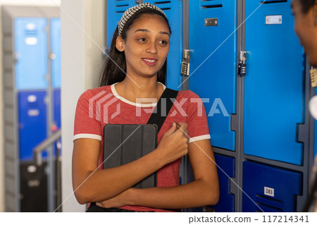 In high school, teenage girl holding tablet and talking near lockers In high school, teenage girl holding tablet and talking near lockers 117214341