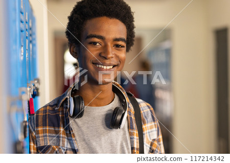 Smiling teenager with headphones standing by lockers in high school hallway Smiling teenager with headphones standing by lockers in high school hallway 117214342