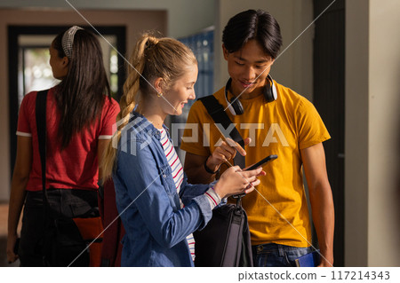 Teenagers in high school hallway looking at smartphone and smiling together Teenagers in high school hallway looking at smartphone and smiling together 117214343