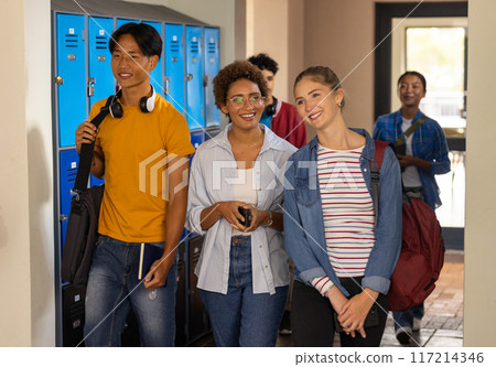 Walking in high school hallway, teenagers smiling and carrying backpacks 117214346