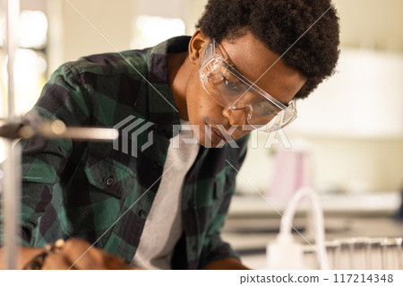 Wearing safety goggles, teenager conducting science experiment in high school classroom Wearing safety goggles, teenager conducting science experiment in high school classroom 117214348