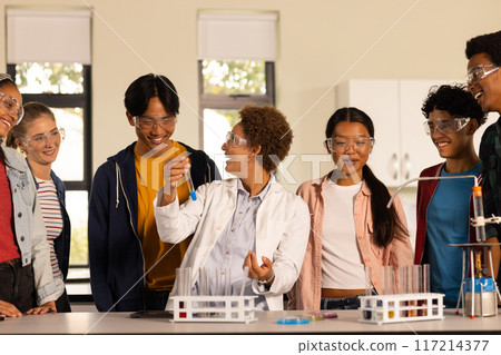 Wearing safety goggles, students conducting science experiment in high school classroom 117214377
