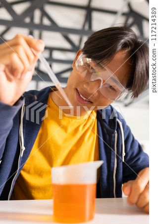 Conducting science experiment, teenager using pipette and beaker in high school lab 117214389