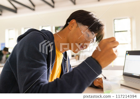 In high school, teenager conducting science experiment with laptop and safety goggles In high school, teenager conducting science experiment with laptop and safety goggles 117214394