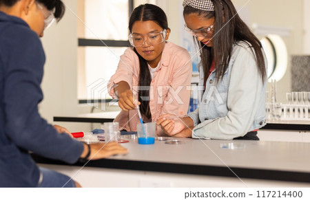 In high school, teenagers conducting science experiment with safety goggles in classroom 117214400