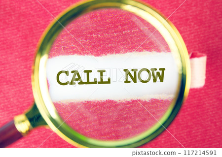Conceptual call now symbol. Copy space. Call now message written through a magnifying glass under a torn paper 117214591