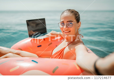 Woman laptop sea. Freelancer woman in sunglases floating on an inflatable big pink donut with a laptop in the sea. People summer vacation rest lifestyle concept 117214677