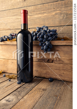 Bottle of red wine with blue grapes on a wooden table. 117215584