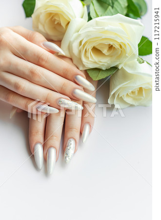 Female Hands with beautiful pearl manicure and white roses. Female Hands with beautiful pearl manicure and white roses. 117215941