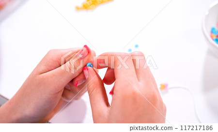 Delicate fingers of a young girl navigate through a treasure trove of bright, multicolored beads, each compartment revealing a new hue to choose from. She's immersed in the joyful task of stringing Delicate fingers of a young girl navigate through a treasure trove of bright, multicolored beads, each compartment revealing a new hue to choose from. She's immersed in the joyful task of stringing 117217186