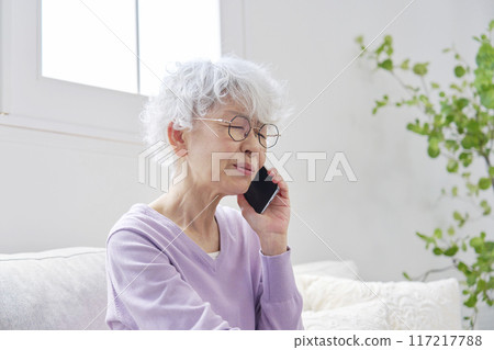Senior woman having trouble talking on a smartphone in the living room 117217788