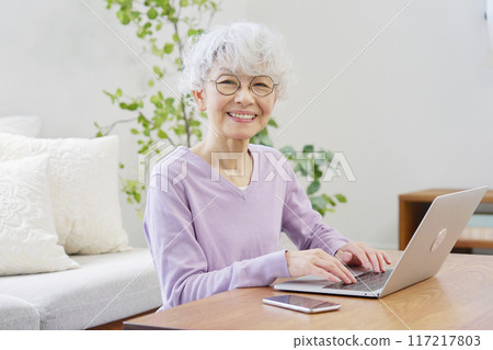 Senior woman using laptop in living room looking at camera 117217803