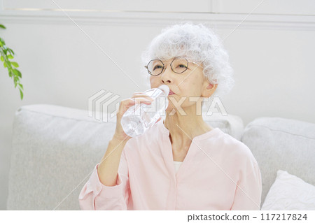 Senior woman holding a bottle of water in the living room Senior woman holding a bottle of water in the living room 117217824