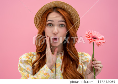 Cute young woman in straw hat with a flower in hands looking surprised Cute young woman in straw hat with a flower in hands looking surprised 117218065