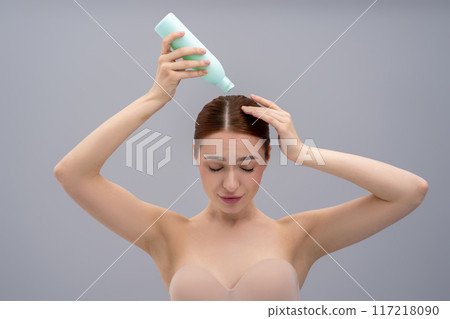 Young ginger woman using anti-dandruff shampoo while washing her hair Young ginger woman using anti-dandruff shampoo while washing her hair 117218090