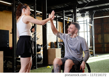 Side view portrait of young man with disability high five with female coach after successful training in gym Side view portrait of young man with disability high five with female coach after successful training in gym 117218172