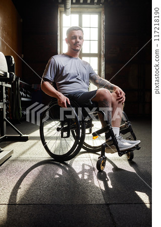 Vertical full length portrait of young man using wheelchair in gym lit by sunlight 117218190