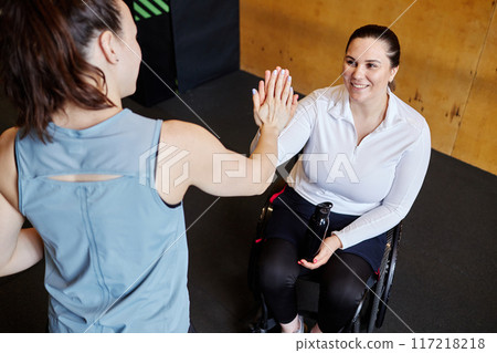 High angle view of smiling woman with disability fist bump with female fitness trainer after successful workout in gym 117218218
