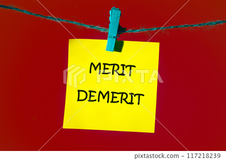 Merit, demerit and its retributions at the level of the individual. MERIT DEMERIT words on a yellow sticker on a rope with a clothespin on a rich red background Merit, demerit and its retributions at the level of the individual. MERIT DEMERIT words on a yellow sticker on a rope with a clothespin on a rich red background 117218239