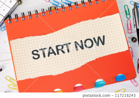 Business marketing, motivational start now concept. Copy space. Start now symbol on a piece of paper on a notebook Business marketing, motivational start now concept. Copy space. Start now symbol on a piece of paper on a notebook 117218243