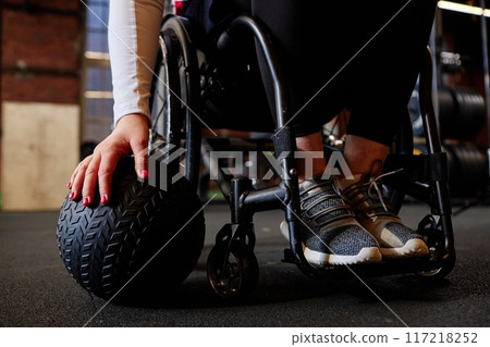 Close up of unrecognizable woman using wheelchair in gym and doing exercises with medball copy space 117218252