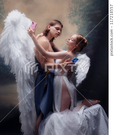 Man and woman, angels, holding smartphones while embracing against vintage background. Social media, dating apps. Blend of classic and modern love 117218557