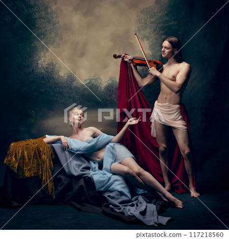 Man playing violin for young tender woman draped in blue fabric against vintage background. Sense of romance, creativity and admiration. 117218560