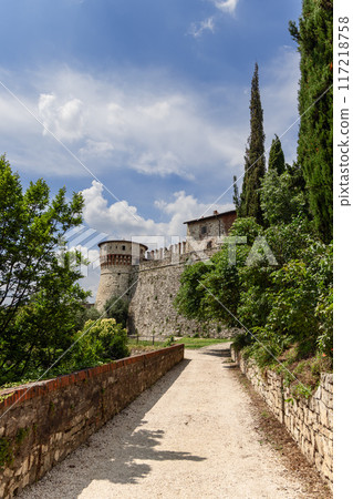 Pathway in Brescia castle park with lush greenery, historic stone walls, and Torre dei Prigionieri 117218758