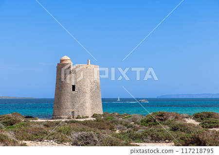 Torre de ses Portes in Ibiza overlooking blue waters, where a sailboat and tour boat navigate Torre de ses Portes in Ibiza overlooking blue waters, where a sailboat and tour boat navigate 117218795