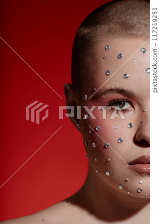 Vertical half portrait of young woman wearing make up with gems looking at camera on red background Vertical half portrait of young woman wearing make up with gems looking at camera on red background 117219251