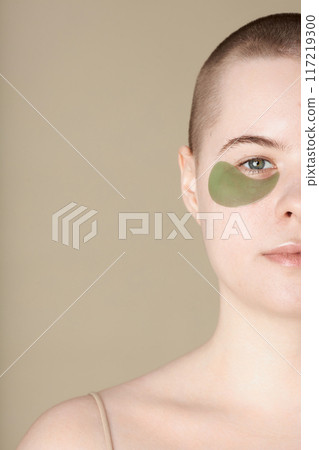 Minimal half portrait of youthful girl wearing moisturizing eye patch looking at camera on beige background copy space Minimal half portrait of youthful girl wearing moisturizing eye patch looking at camera on beige background copy space 117219300