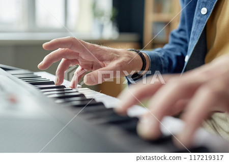 Close up of unrecognizable senior man playing piano at home with focus on hands and keys copy space 117219317