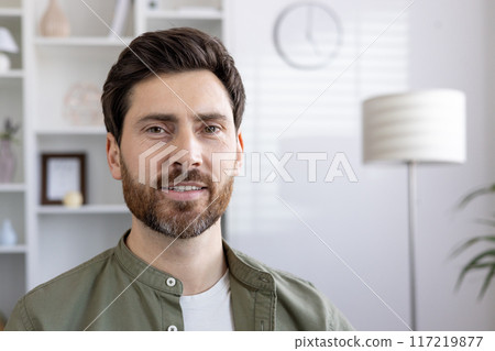 Smiling bearded man in casual clothes looking at camera in bright room. Positive expression and relaxed demeanor convey friendliness and approachability. Professional and casual mix for versatile uses 117219877